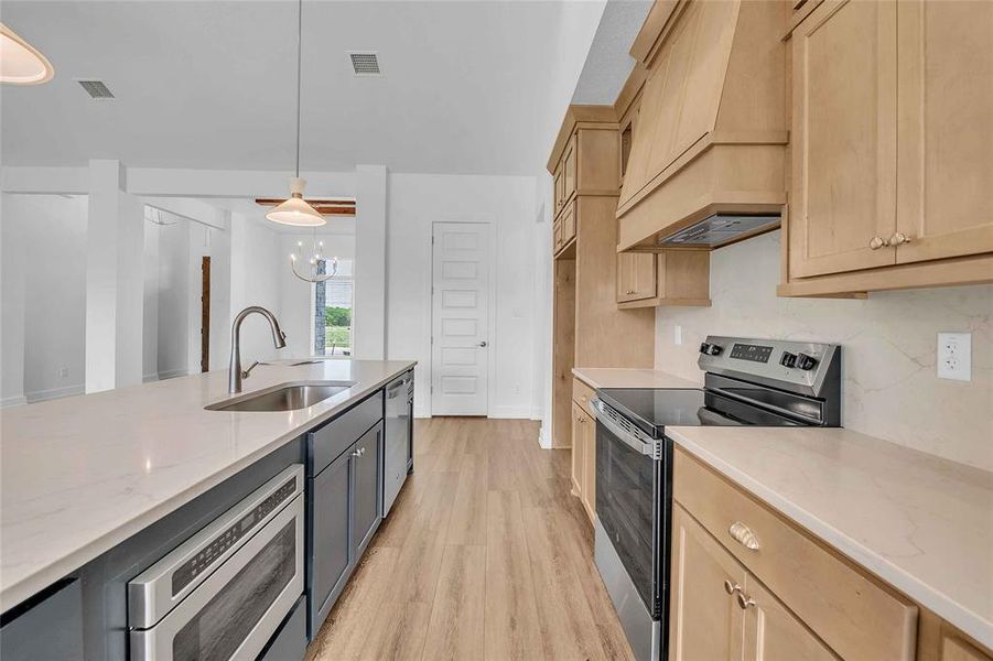 Kitchen with appliances with stainless steel finishes, light stone countertops, a sink, custom range hood, and light wood-style flooring