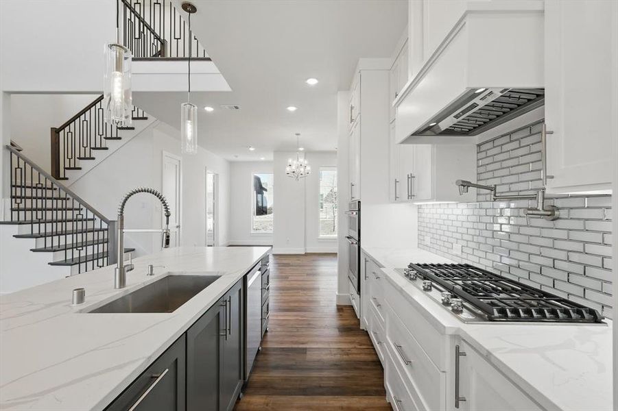 Kitchen with stainless steel appliances, a sink, white cabinetry, hanging light fixtures, and custom exhaust hood