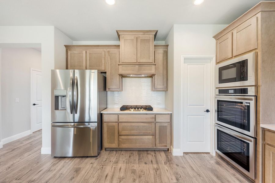 Kitchen with light wood cabinets, stainless steel appliances, double wall oven, and hardwood floors
