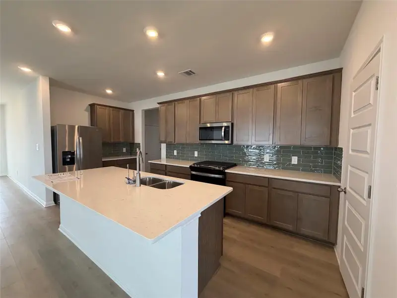 Kitchen featuring tasteful backsplash, light stone counters, appliances with stainless steel finishes, light wood finished floors, and a center island with sink