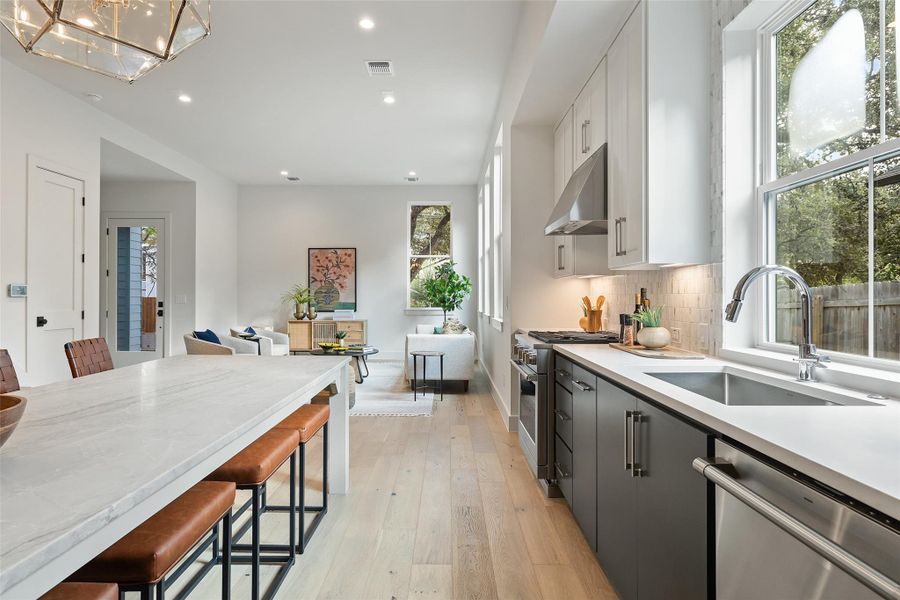 Kitchen with appliances with stainless steel finishes, sink, white cabinets, gray cabinetry, and a breakfast bar area