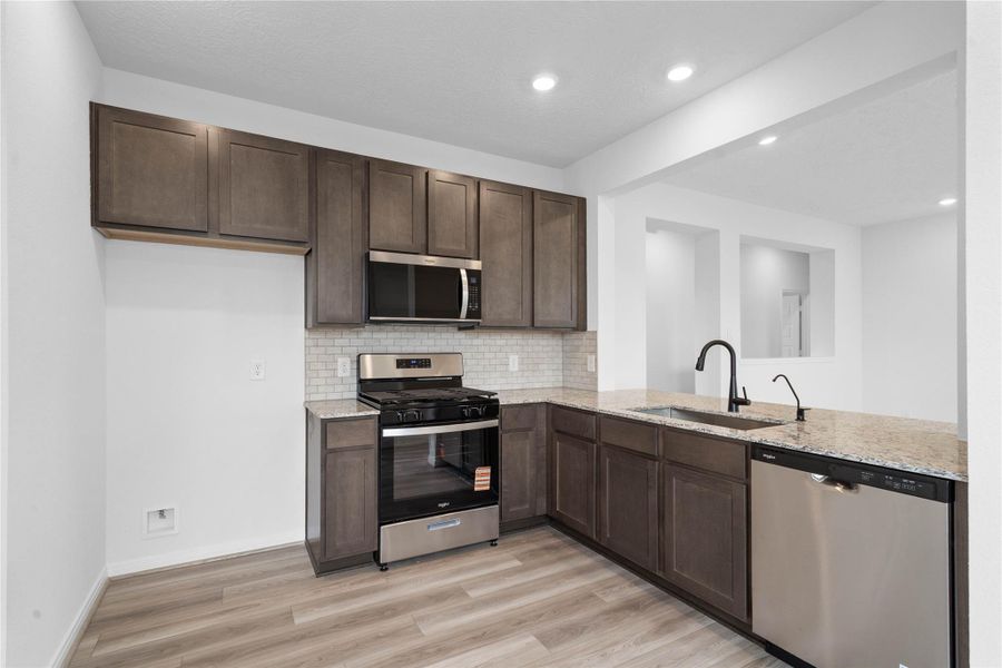 Efficiently designed kitchen maximizes every inch of space, with Woodmont Dakota cabinetry in Smolder, Whirlpool stainless steel appliances, and granite countertops. The perfect functional hub for daily cooking.