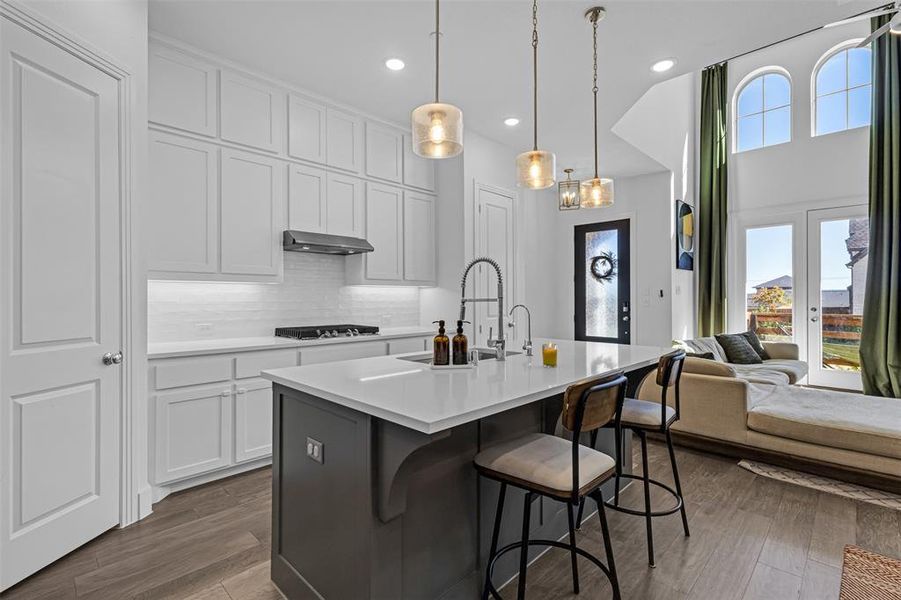 Kitchen featuring tasteful backsplash, a center island with sink, a kitchen breakfast bar, dark wood-style floors, and hanging light fixtures