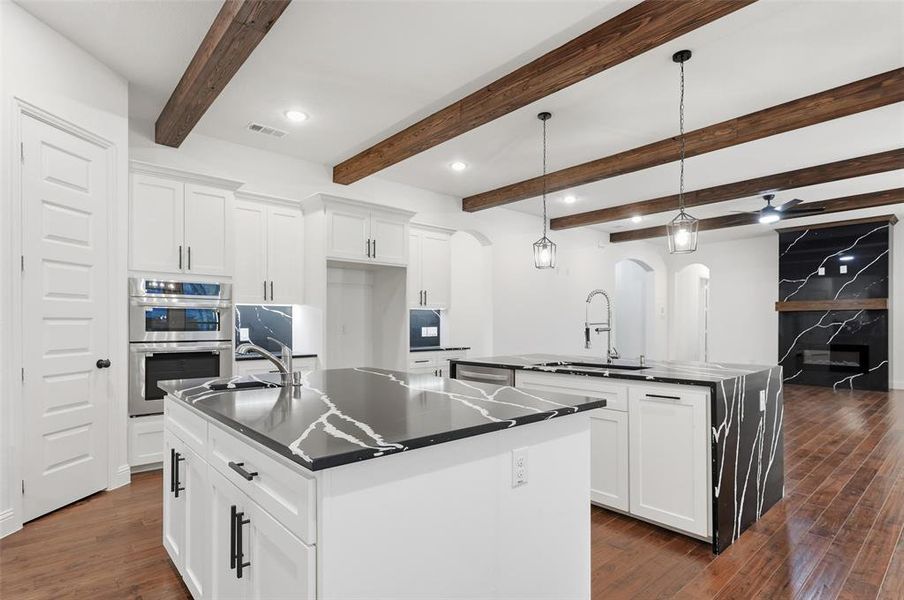 Kitchen with arched walkways, white cabinets, hanging light fixtures, beamed ceiling, and recessed lighting