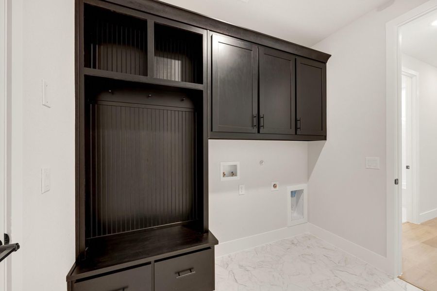 Laundry room with dark wood built-in cabinets, open shelving, and marble tile floors with washer and dryer hookups. Laundry room with dark wood built-in cabinets, open shelving, and marble tile floors with washer and dryer hookups.