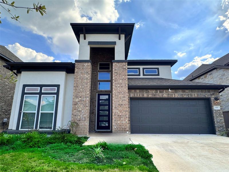 View of front facade featuring brick siding, concrete driveway, stucco siding, and an attached garage