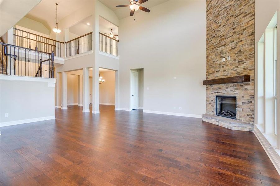 Unfurnished living room featuring a towering ceiling, a fireplace, ceiling fan with notable chandelier, and dark hardwood / wood-style flooring