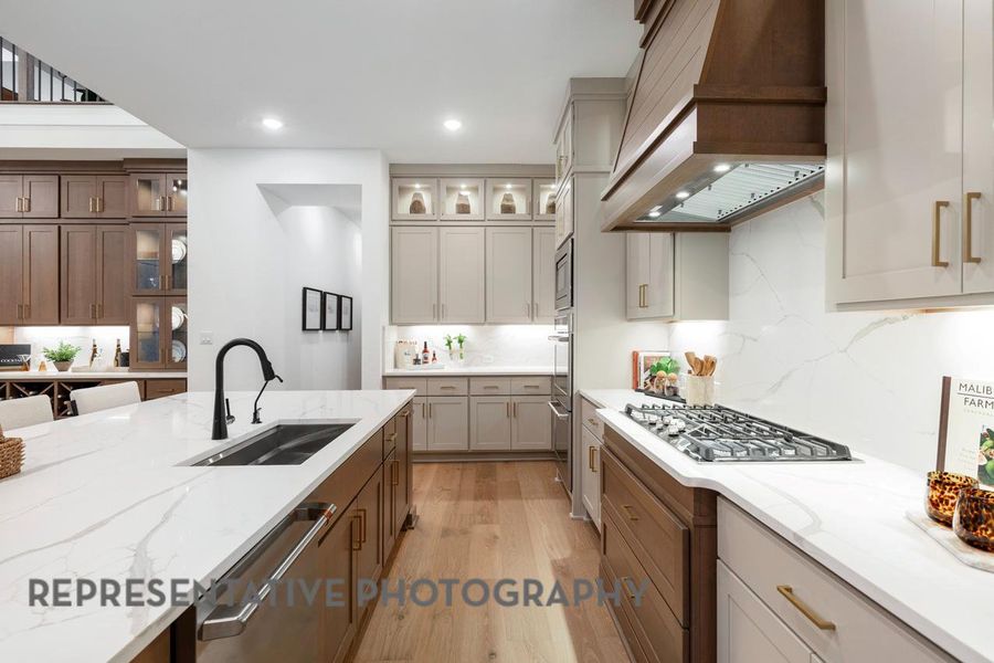 Kitchen with custom range hood, a sink, stainless steel appliances, light wood-style flooring, and light stone countertops Kitchen with custom range hood, a sink, stainless steel appliances, light wood-style flooring, and light stone countertops