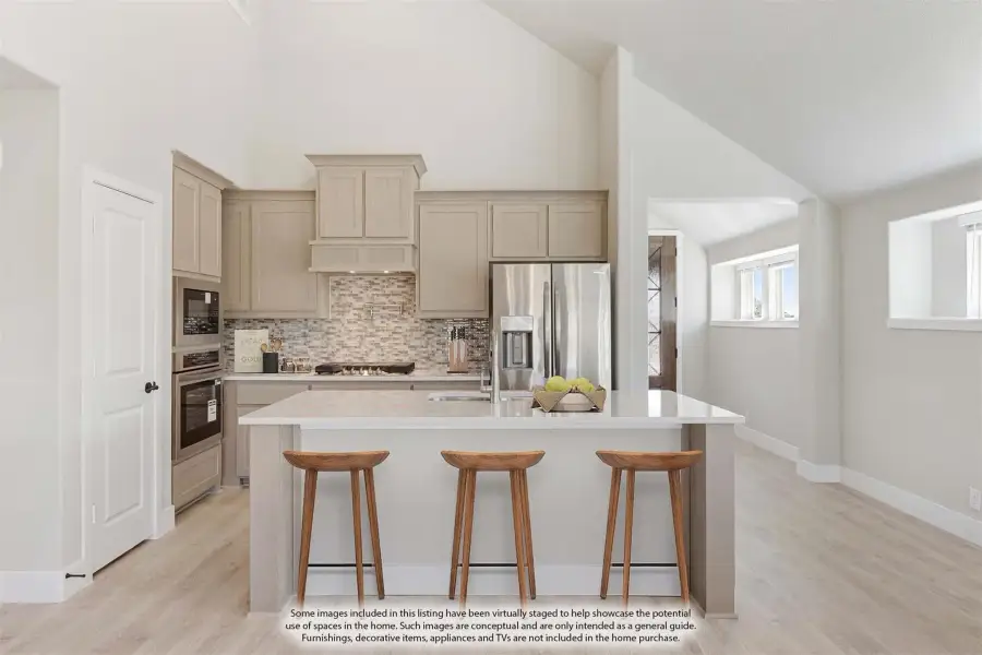Kitchen with tan cabinets, tile backsplash, stainless appliances, and island with three bar stools