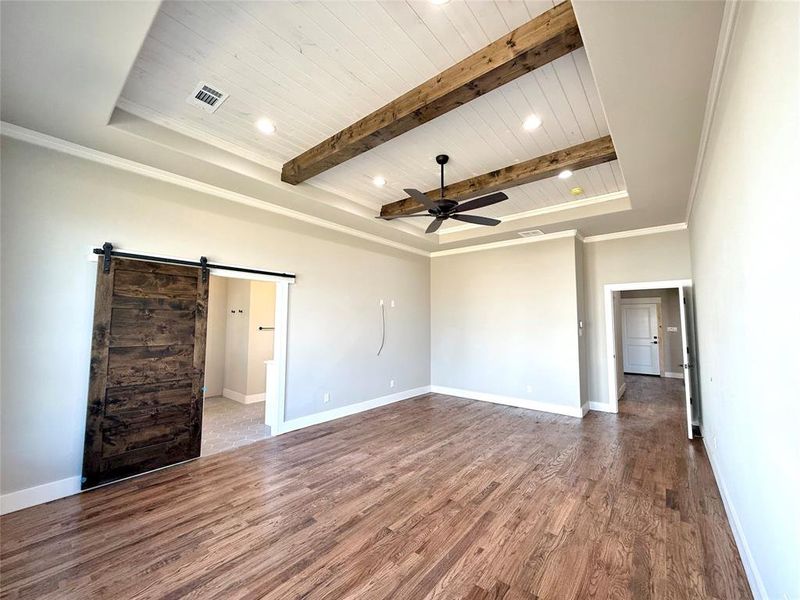 Unfurnished bedroom with a barn door, a wooden ceiling with exposed beams, dark wood-style floors, ceiling fan, and connected bathroom Unfurnished bedroom with a barn door, a wooden ceiling with exposed beams, dark wood-style floors, ceiling fan, and connected bathroom