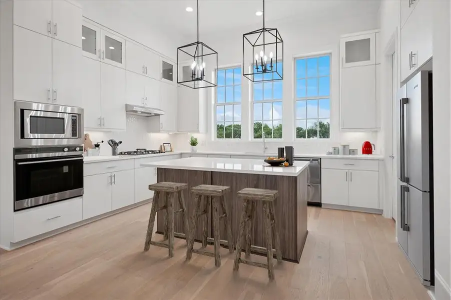Kitchen featuring glass fronted cabinets, a breakfast bar, stainless steel appliances, a center island, and light wood finished floors