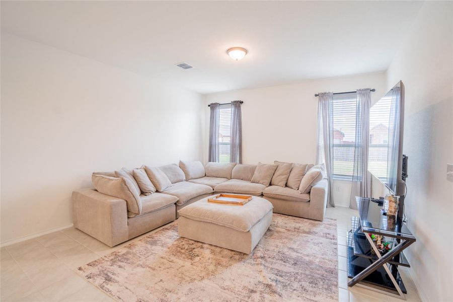 Spacious living area featuring light-toned walls, tile flooring, and multiple windows with blinds Spacious living area featuring light-toned walls, tile flooring, and multiple windows with blinds