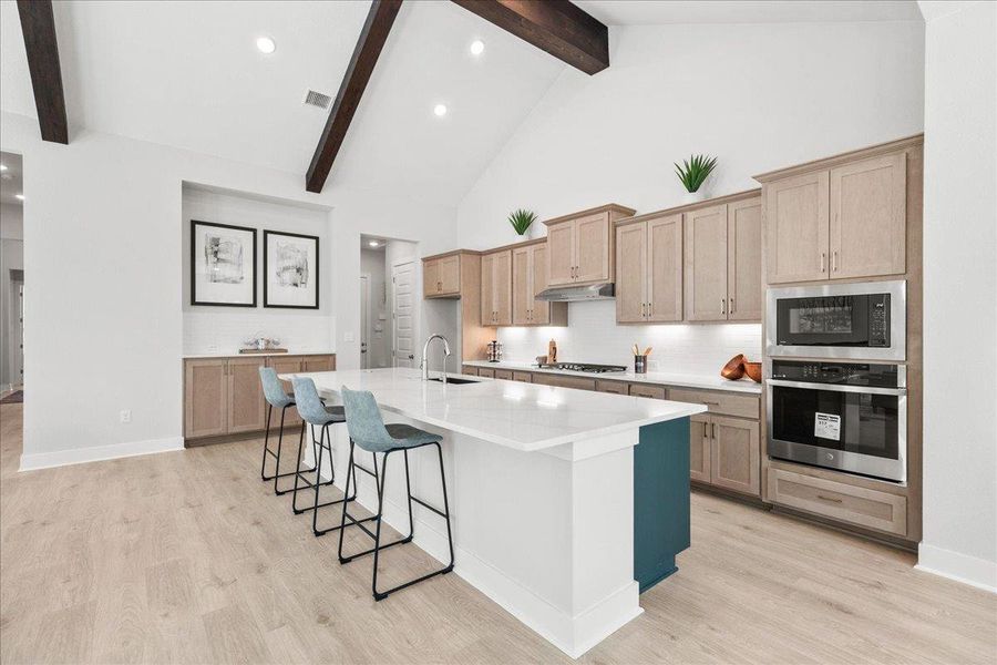 Kitchen featuring decorative backsplash, appliances with stainless steel finishes, light brown cabinets, a breakfast bar, and beam ceiling