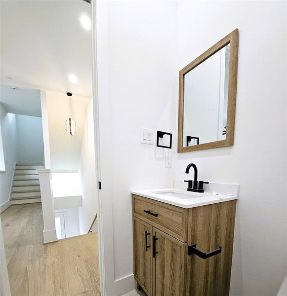 This photo shows a modern, clean bathroom featuring a combination bathtub and shower with sleek black fixtures, a large rectangular mirror above a white sink with a black faucet, and light wood cabinetry. The space is finished with large gray tiles and has a bright, minimalist aesthetic.