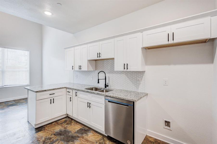 Kitchen featuring stainless steel dishwasher, tasteful backsplash, white cabinets, sink, and dark tile patterned flooring