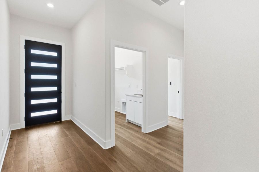 A welcoming entry hall with natural wood flooring leads to a functional utility room. A welcoming entry hall with natural wood flooring leads to a functional utility room.