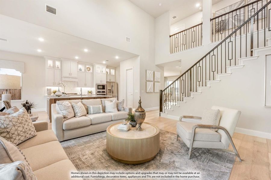 Open living room with high ceilings, staircase, and open kitchen visible in the background, hardwood floors throughout