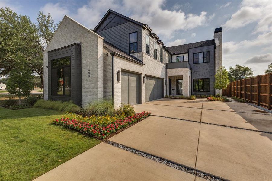Contemporary residence featuring a light brick and dark siding facade, a segmented concrete driveway, and integrated garage doors Contemporary residence featuring a light brick and dark siding facade, a segmented concrete driveway, and integrated garage doors