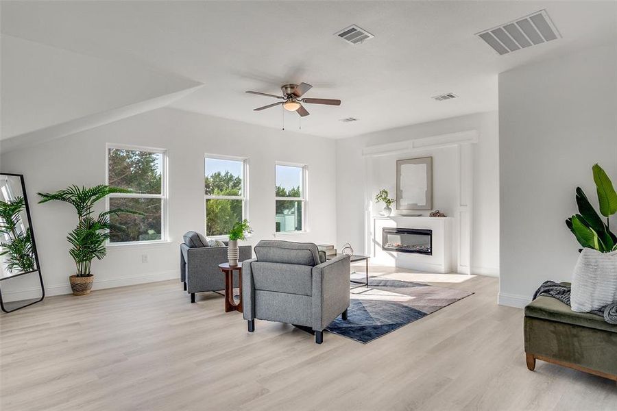 Living area featuring light wood-style flooring, ceiling fan, and a glass covered fireplace Living area featuring light wood-style flooring, ceiling fan, and a glass covered fireplace