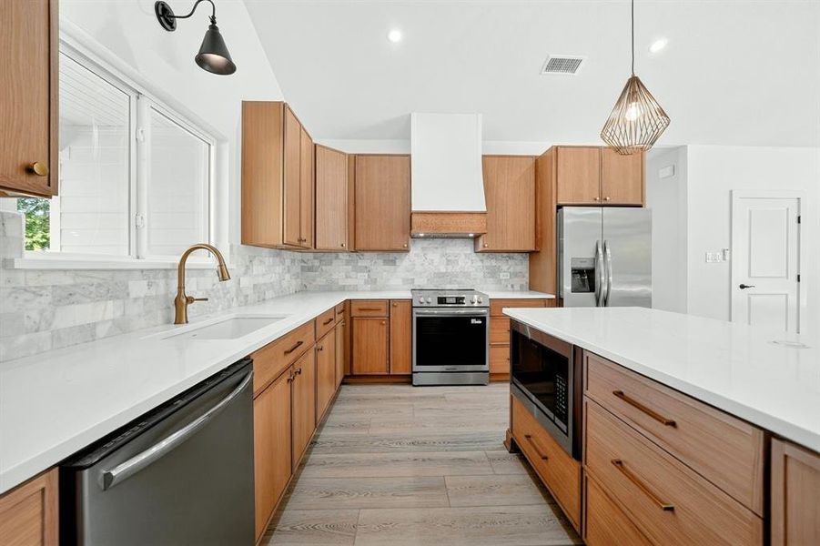 Modern kitchen featuring wood-finish cabinetry, stainless steel appliances, a white quartz countertop, a subway tile backsplash, and wood-finish flooring