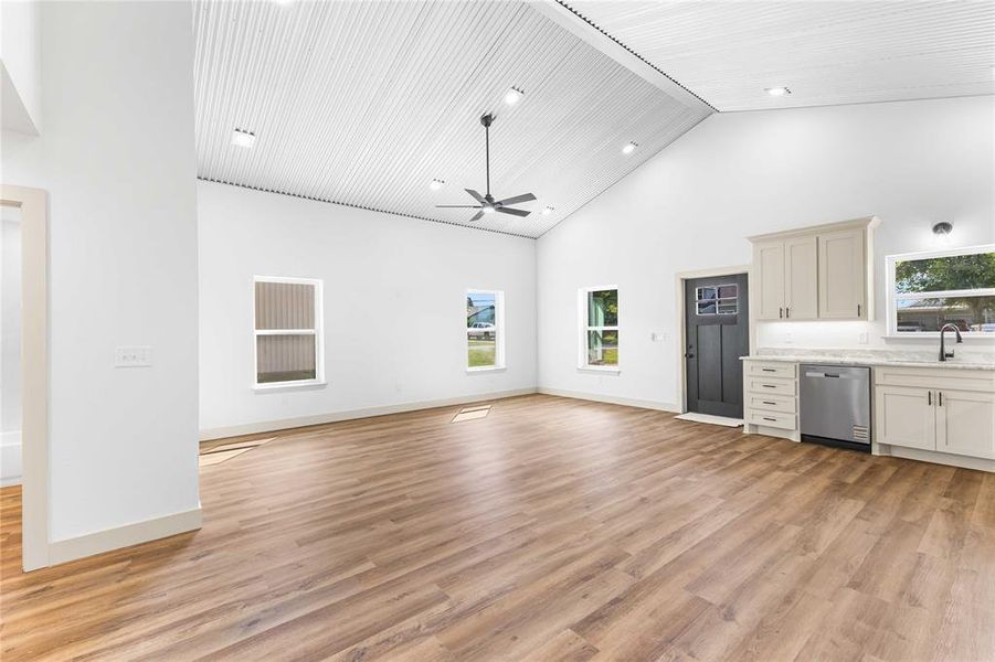 Bar area with high vaulted ceiling, light wood-style floors, dishwasher, light stone counters, and ceiling fan Bar area with high vaulted ceiling, light wood-style floors, dishwasher, light stone counters, and ceiling fan