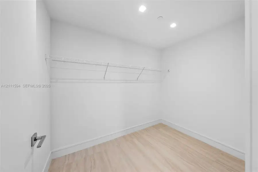 Walk-in closet featuring light wood-finish flooring, white walls, recessed ceiling lighting, and white wire shelving Walk-in closet featuring light wood-finish flooring, white walls, recessed ceiling lighting, and white wire shelving