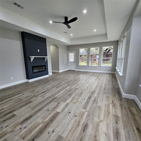large fireplace, light wood finished floors, arched walkways, recessed lighting, and a tray ceiling