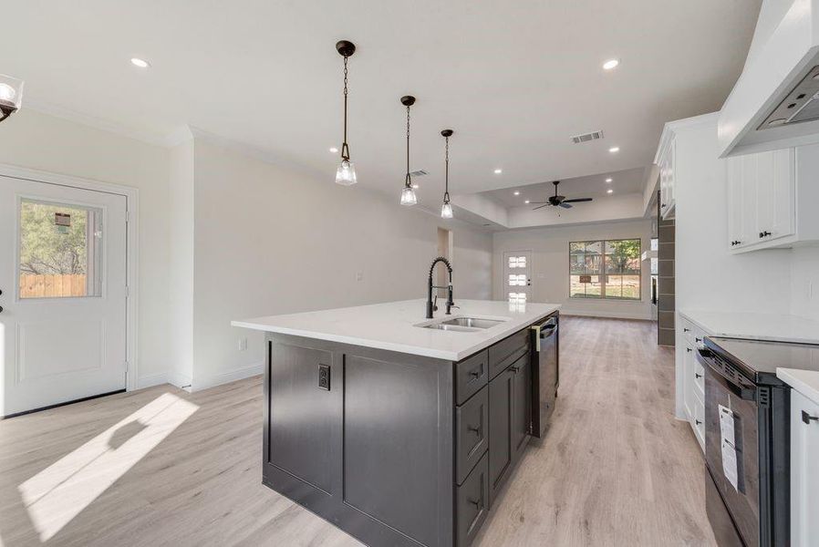 Kitchen featuring sink, an island with sink, white cabinetry, light hardwood / wood-style floors, and pendant lighting