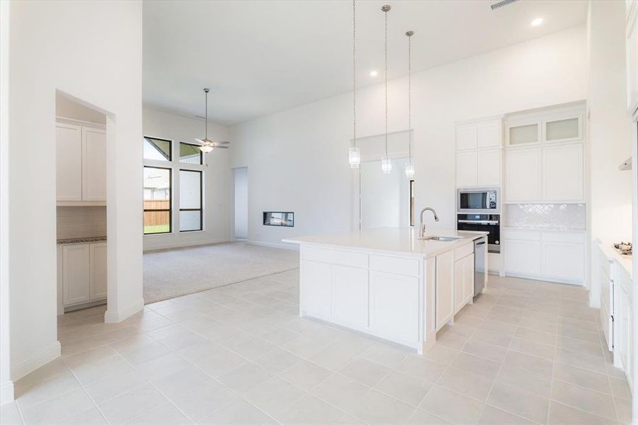 Kitchen featuring decorative light fixtures, backsplash, oven, a center island with sink, and stainless steel microwave