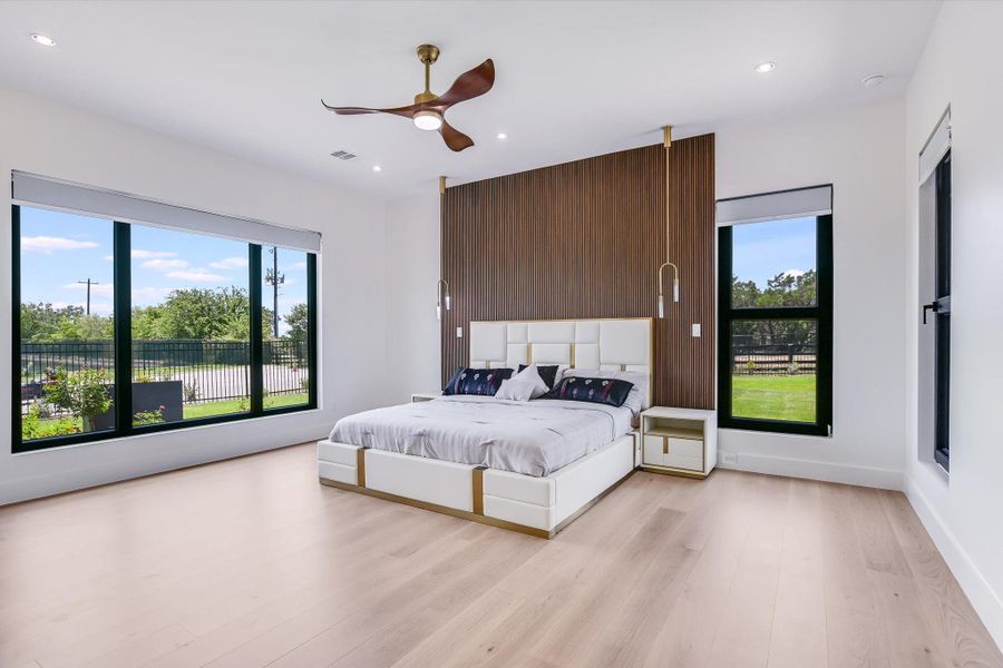 Primary Bedroom on main floor with large windows, light wood-style flooring, wood accent wall, custom sconce lighting as well as recessed lighting, and ceiling fan Primary Bedroom on main floor with large windows, light wood-style flooring, wood accent wall, custom sconce lighting as well as recessed lighting, and ceiling fan
