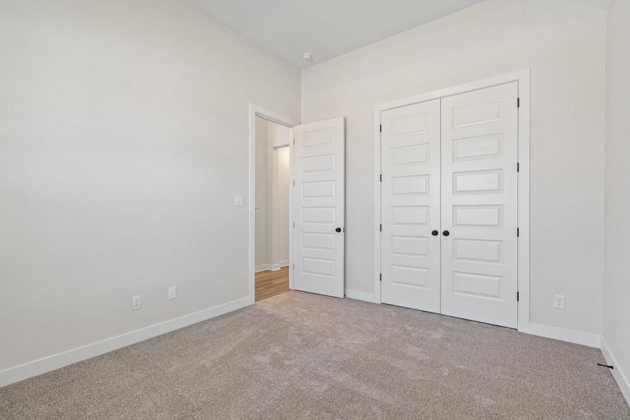 Neutral-toned carpeted room featuring a double-door closet with panel doors and matte black hardware Neutral-toned carpeted room featuring a double-door closet with panel doors and matte black hardware