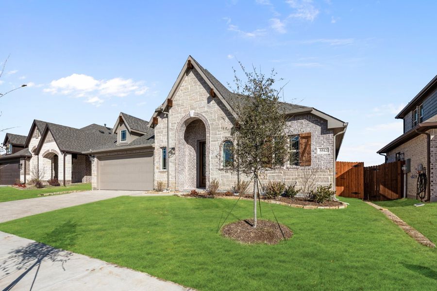 Single-story home with stone and brick exterior, arched entry, two-car garage, and green front lawn Single-story home with stone and brick exterior, arched entry, two-car garage, and green front lawn