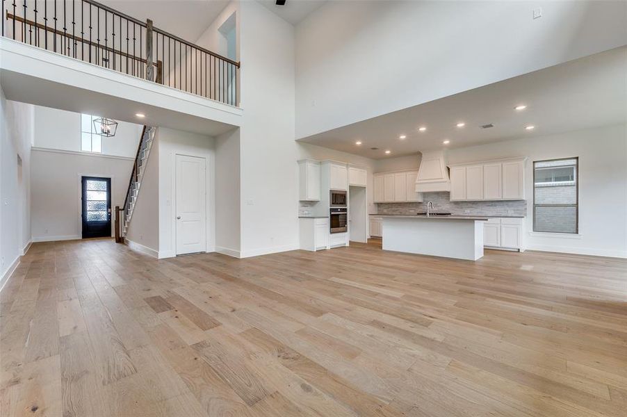 Unfurnished living room with sink, light hardwood / wood-style floors, and a high ceiling