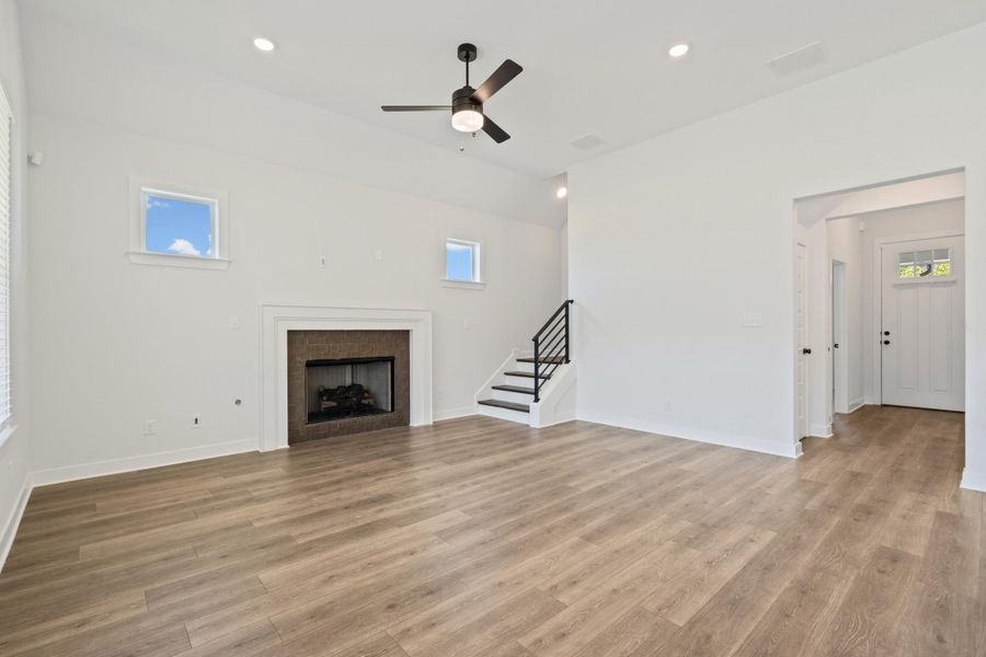 Spacious interior featuring wood-finish flooring, a fireplace with a stone surround, and a ceiling fan with integrated lighting Spacious interior featuring wood-finish flooring, a fireplace with a stone surround, and a ceiling fan with integrated lighting