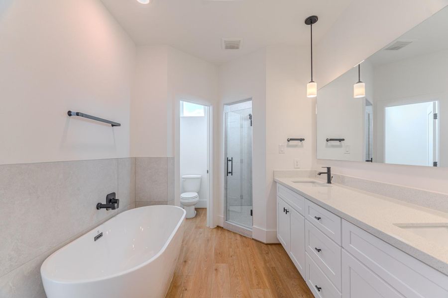 This modern bathroom features a freestanding bathtub, a spacious glass-enclosed shower, and a double vanity with ample counter space. Bright lighting and sleek fixtures enhance the clean, minimalist design, while light wood flooring adds warmth.Photo Disclaimer: Photos are representative of the community and may depict a similar floor plan, model home, or previously completed residence. This modern bathroom features a freestanding bathtub, a spacious glass-enclosed shower, and a double vanity with ample counter space. Bright lighting and sleek fixtures enhance the clean, minimalist design, while light wood flooring adds warmth.Photo Disclaimer: Photos are representative of the community and may depict a similar floor plan, model home, or previously completed residence.