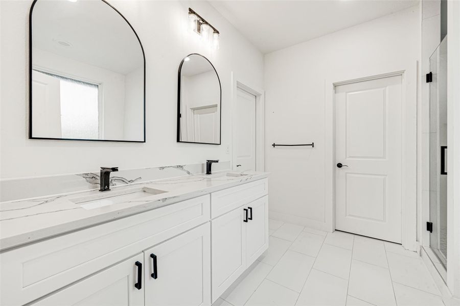 The primary en-suite offers a clean modern design with a large dual-sink vanity. This view highlights the direct access to the expansive walk-in closet and the glass-enclosed shower, creating a functional flow for morning routines.