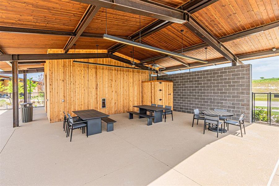Open-air structure featuring a slatted wood ceiling with exposed metal beams, concrete flooring, and a mix of vertical wood paneling and concrete block walls