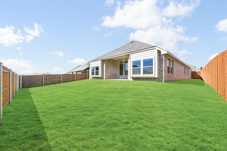 Backyard of single-story brick home with large green lawn and wood privacy fence on both sides.