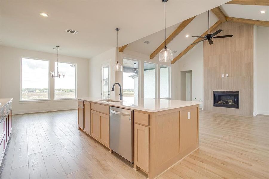 Kitchen with a fireplace, beamed ceiling, sink, a kitchen island with sink, and stainless steel dishwasher