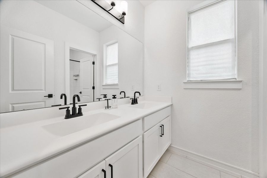 Beautifully designed primary bath showcases oversized walk-in shower, dual vanities, designer tile flooring, and contemporary matte black fixtures.