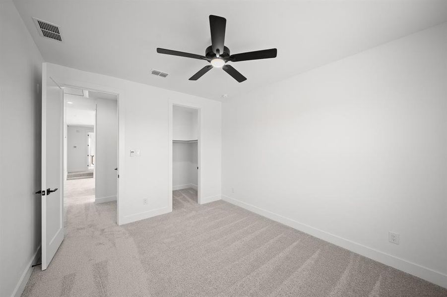 Unfurnished bedroom featuring a spacious closet, light carpet, and ceiling fan