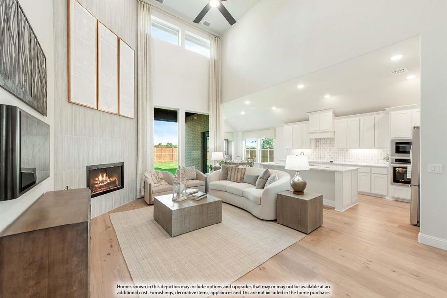 Open-concept living room with two-story ceiling, fireplace, and adjoining white kitchen with hardwood floors