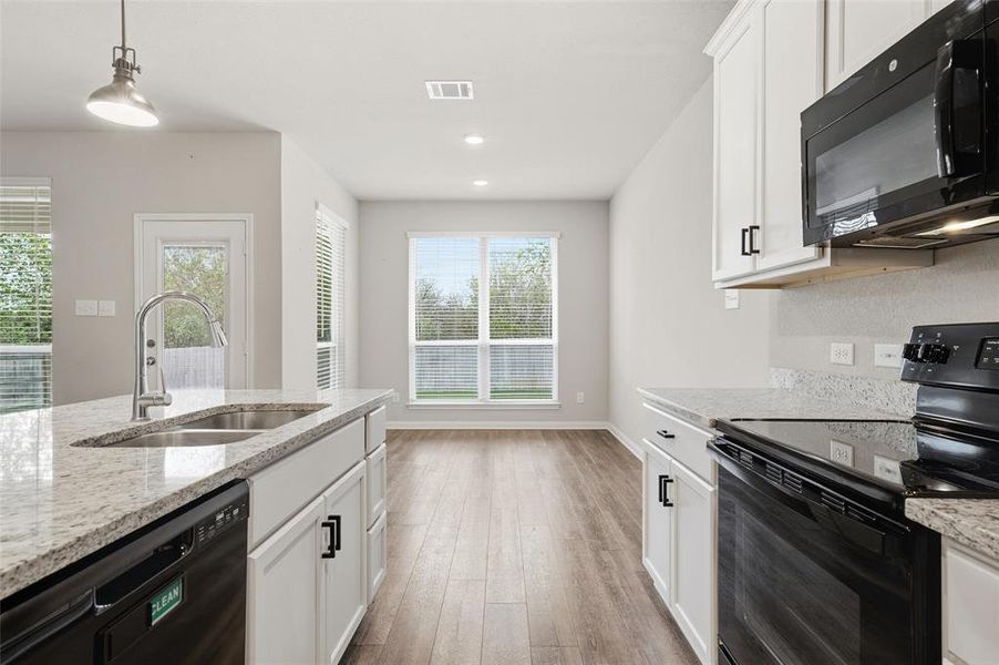 Kitchen with black appliances, white cabinets, pendant lighting, light stone countertops, and light wood finished floors