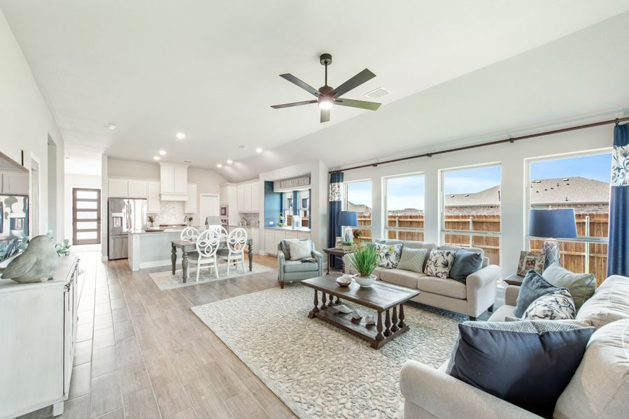 Open-concept living room with vaulted ceiling, ceiling fan, and view into kitchen and dining area