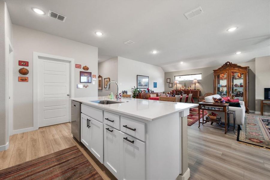 Kitchen with white cabinetry, open floor plan, a center island with sink, light wood-style flooring, and stainless steel dishwasher Kitchen with white cabinetry, open floor plan, a center island with sink, light wood-style flooring, and stainless steel dishwasher