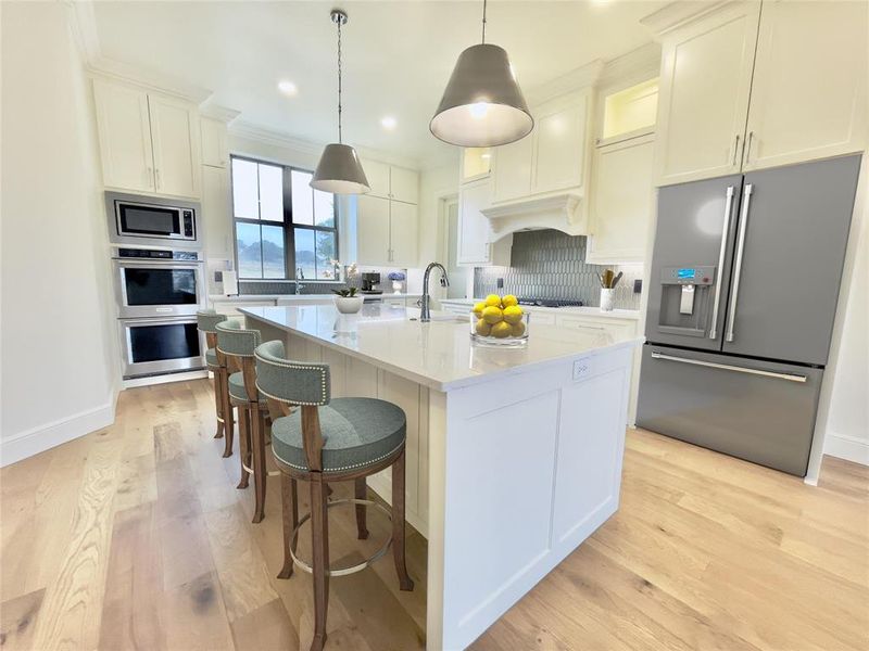 Kitchen featuring an island with sink, tasteful backsplash, light wood-type flooring, and appliances with stainless steel finishes