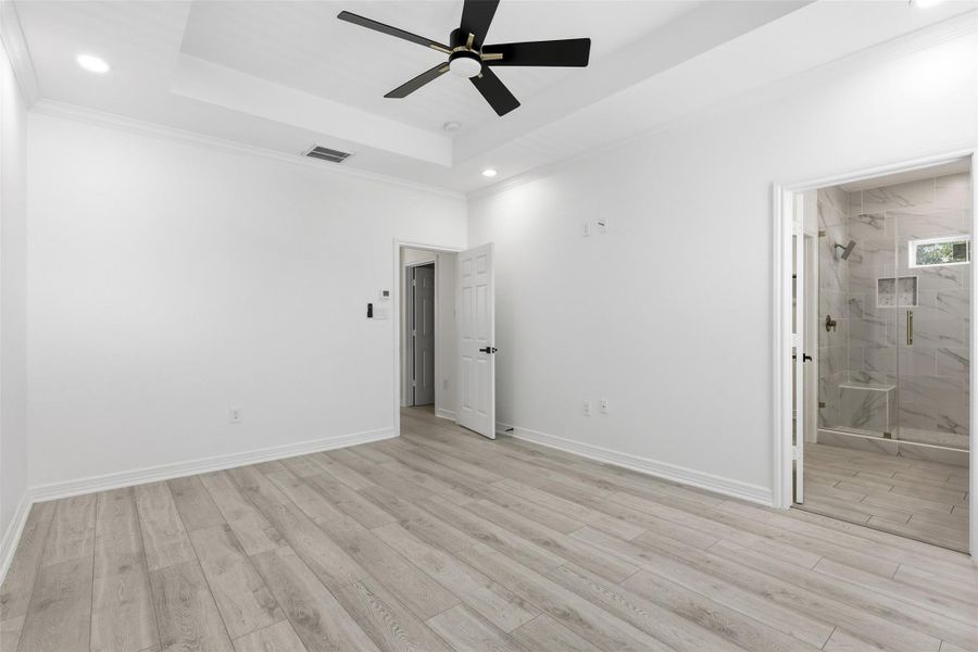 Bright second floor bedroom with ceiling fan, light wood look floors, and attached bathroom access.