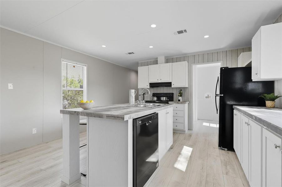Kitchen with white cabinets, black appliances, a kitchen island with sink, recessed lighting, and light countertops Kitchen with white cabinets, black appliances, a kitchen island with sink, recessed lighting, and light countertops