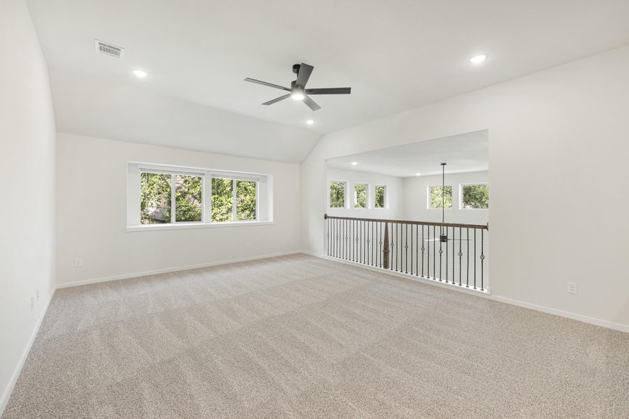 Spacious upstairs bonus room with carpet, vaulted ceiling, ceiling fan, and iron stair railing