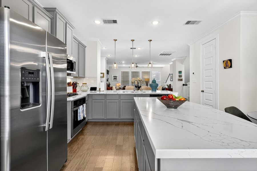 Stylish kitchen featuring stainless steel appliances, gray shaker cabinetry, quartz countertops, and pendant lighting overlooking the dining and living areas. Stylish kitchen featuring stainless steel appliances, gray shaker cabinetry, quartz countertops, and pendant lighting overlooking the dining and living areas.